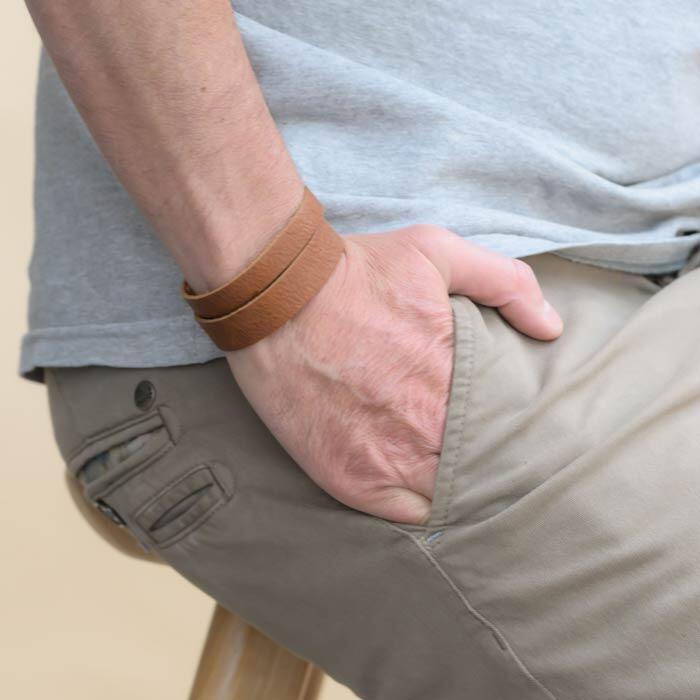 main d'homme dans une poche, au poignet il y a un bracelet en cuir camel